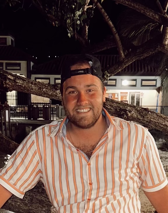 A man in striped shirt and hat standing next to tree.