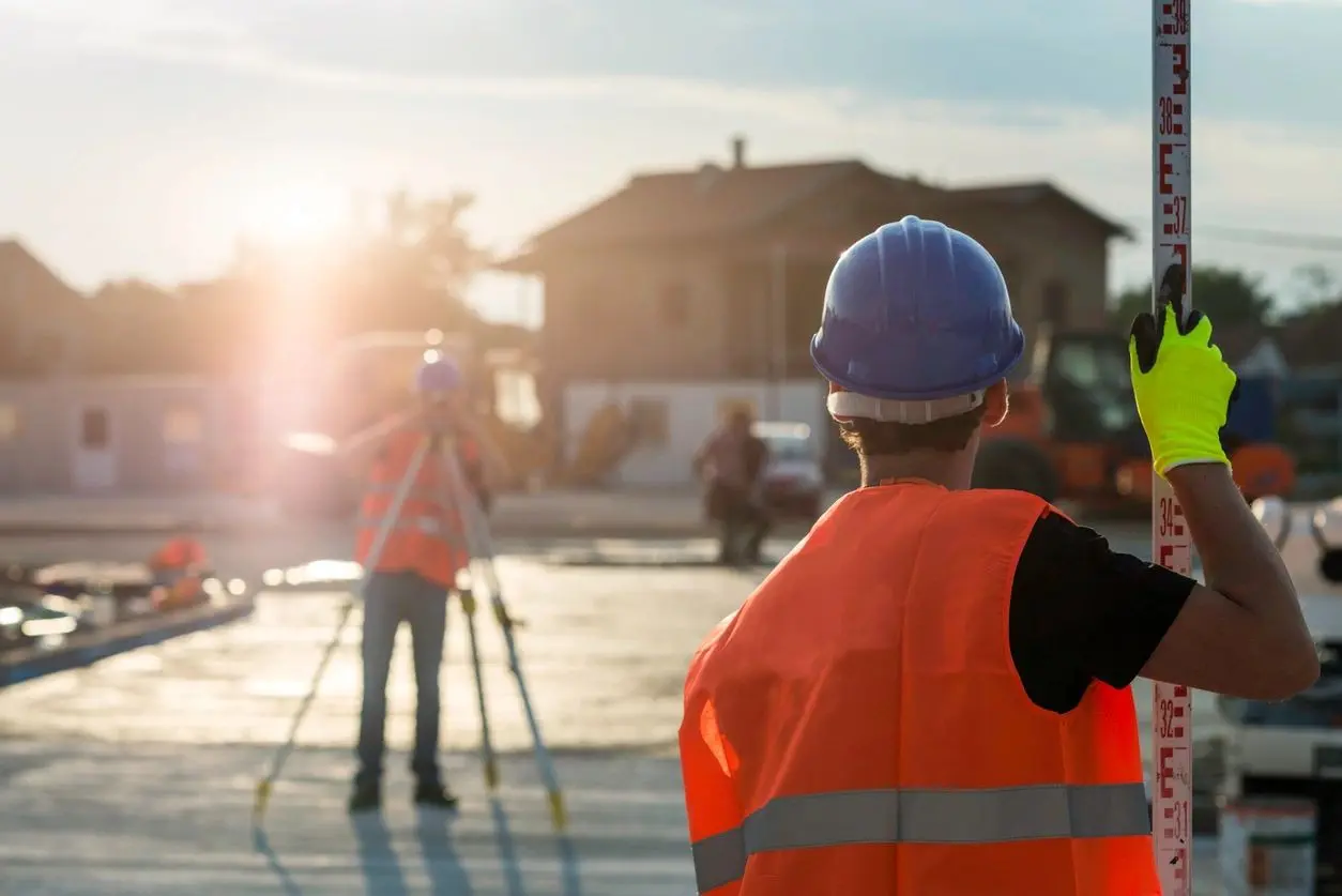 A man in an orange vest and hard hat standing on top of a building.